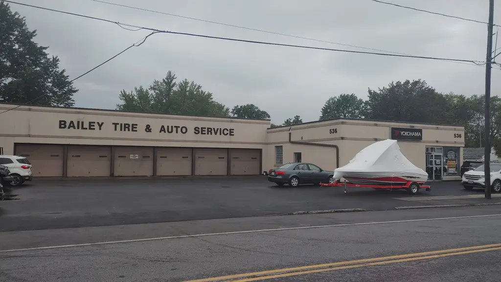 A shrink-wrapped boat on a trailer parked outside Bailey Tire in Buffalo, next to customer cars and a Yokohama tire sign