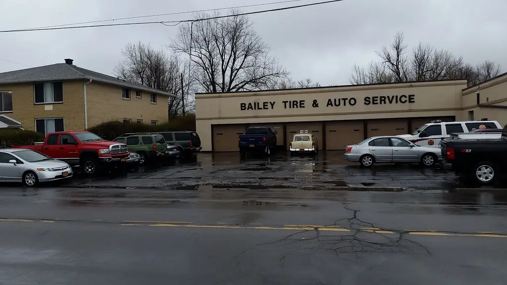 The Bailey Tire exterior storefront on a wet parking lot, with classic and daily-driver customer cars parked out front