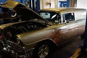 A gold classic wagon with a flame paint job up on a lift inside the Bailey Tire shop, hood open